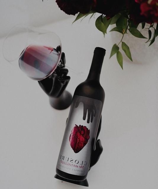 A wine bottle with an artistically designed label sits next to a glass of red wine.